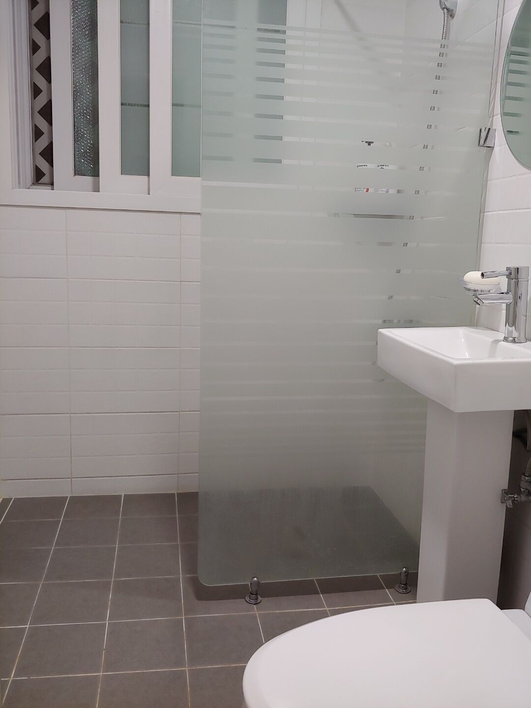 Ein Badezimmer mit Duschkabine aus Glas, einem weißen Waschbecken und einer Toilette.
