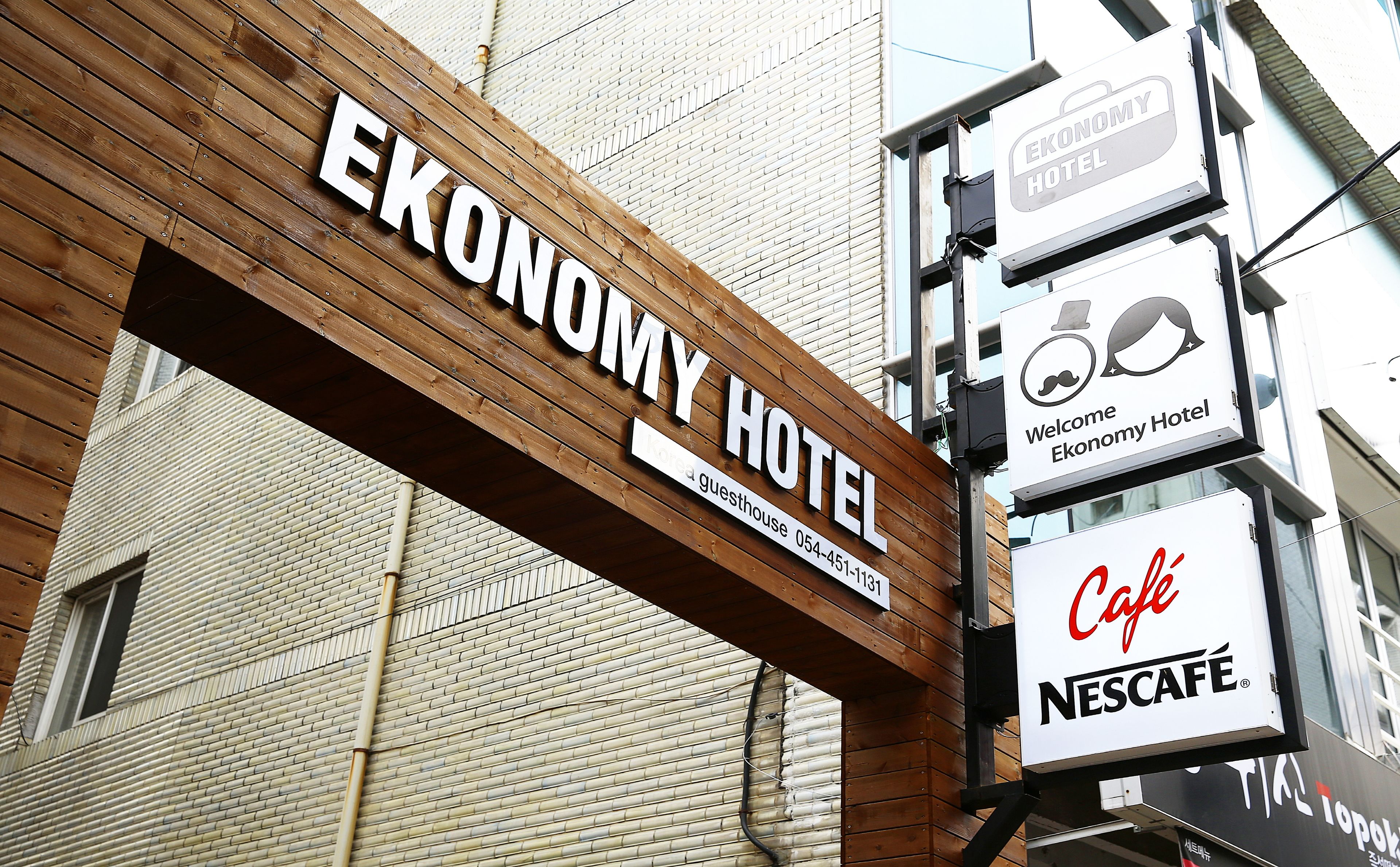 A wooden sign for the Ekonomy Hotel with a guesthouse number and a Nescafe Café sign below.