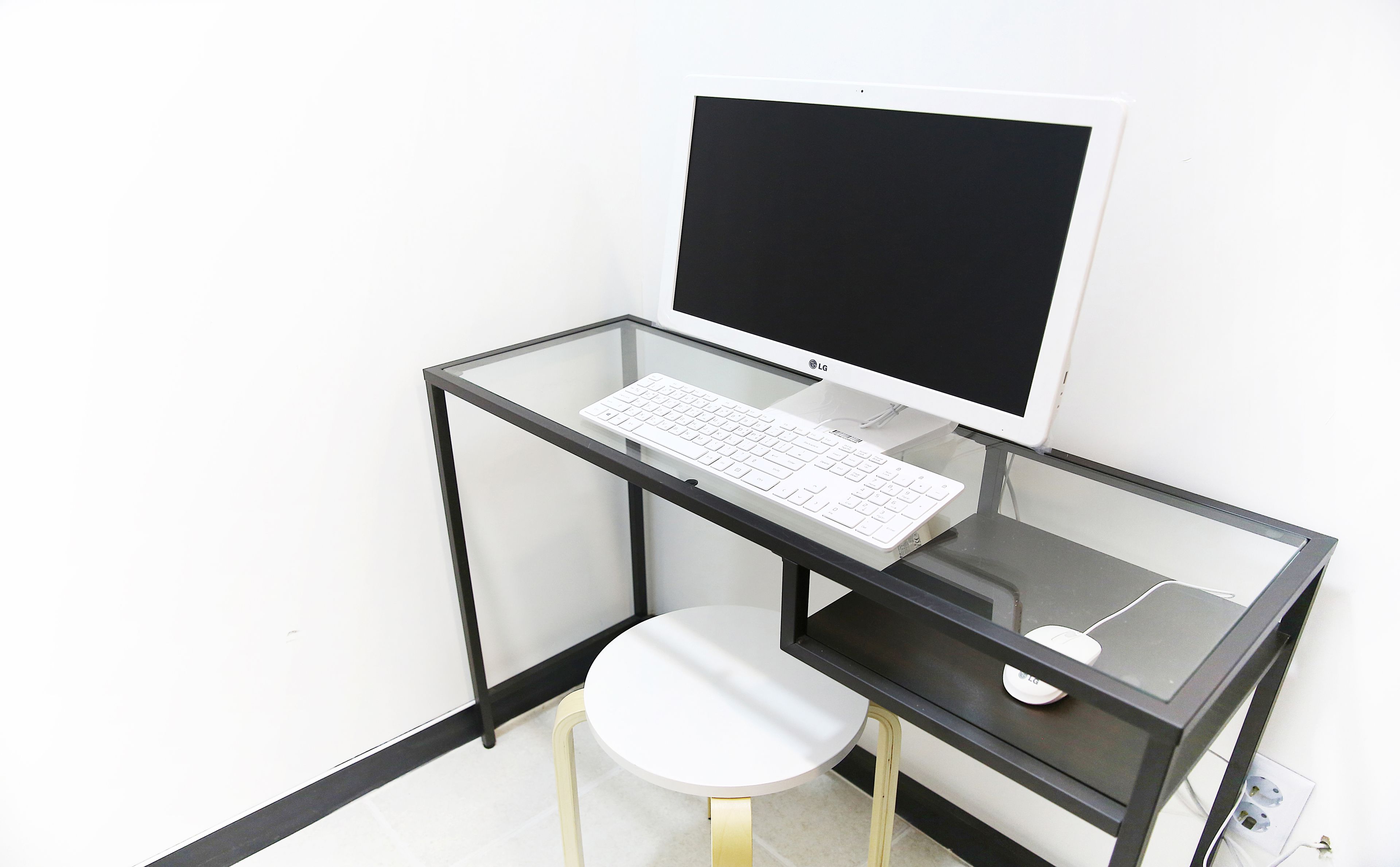 Um espaço de trabalho compacto e moderno com uma mesa de vidro, teclado branco e monitor.