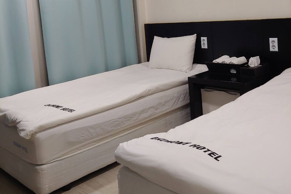 A hotel room with two single beds, a nightstand, and a window with curtains.