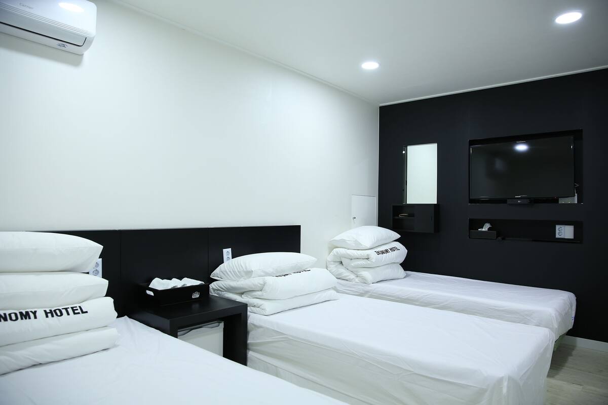 A hotel room with two beds, a black nightstand, a TV, and a mirror on the wall.