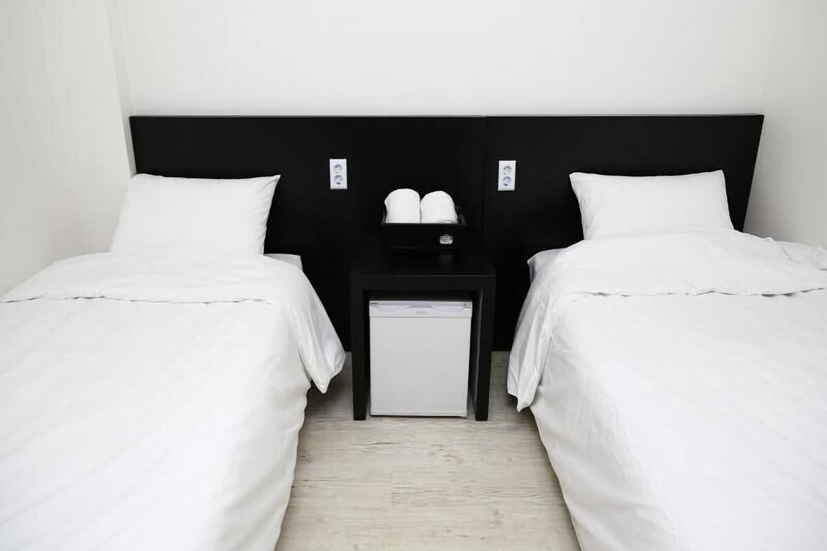 A hotel room with two single beds, a small bedside table, and a nightstand.