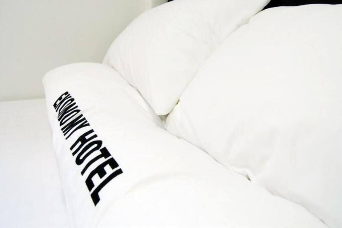 A bed with white bedding and a pillow with the text "EASTWOOD HOTEL" on it.