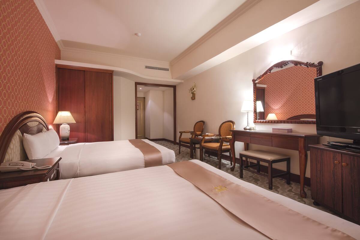 A hotel room with two beds, a desk with a chair, a television, and a desk lamp.