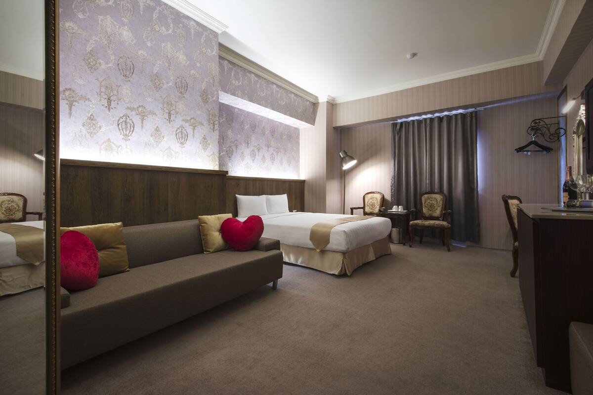 A hotel room with a large bed, a sofa, a desk, and a chair.