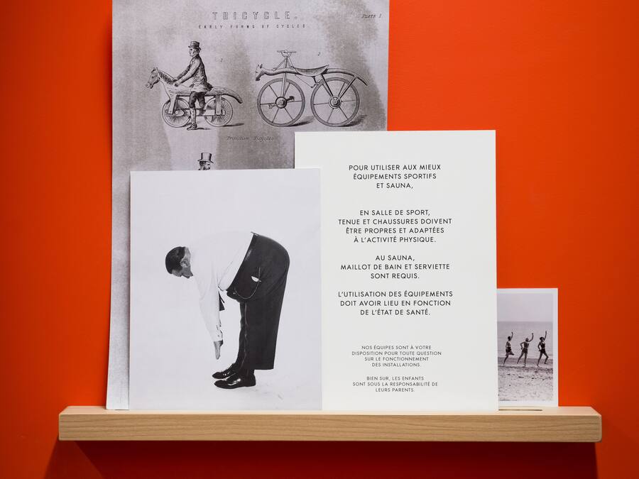 Vintage-Bilder von Fahrrädern und ein Textblatt auf einer Holzablage vor einem orangefarbenen Hintergrund.