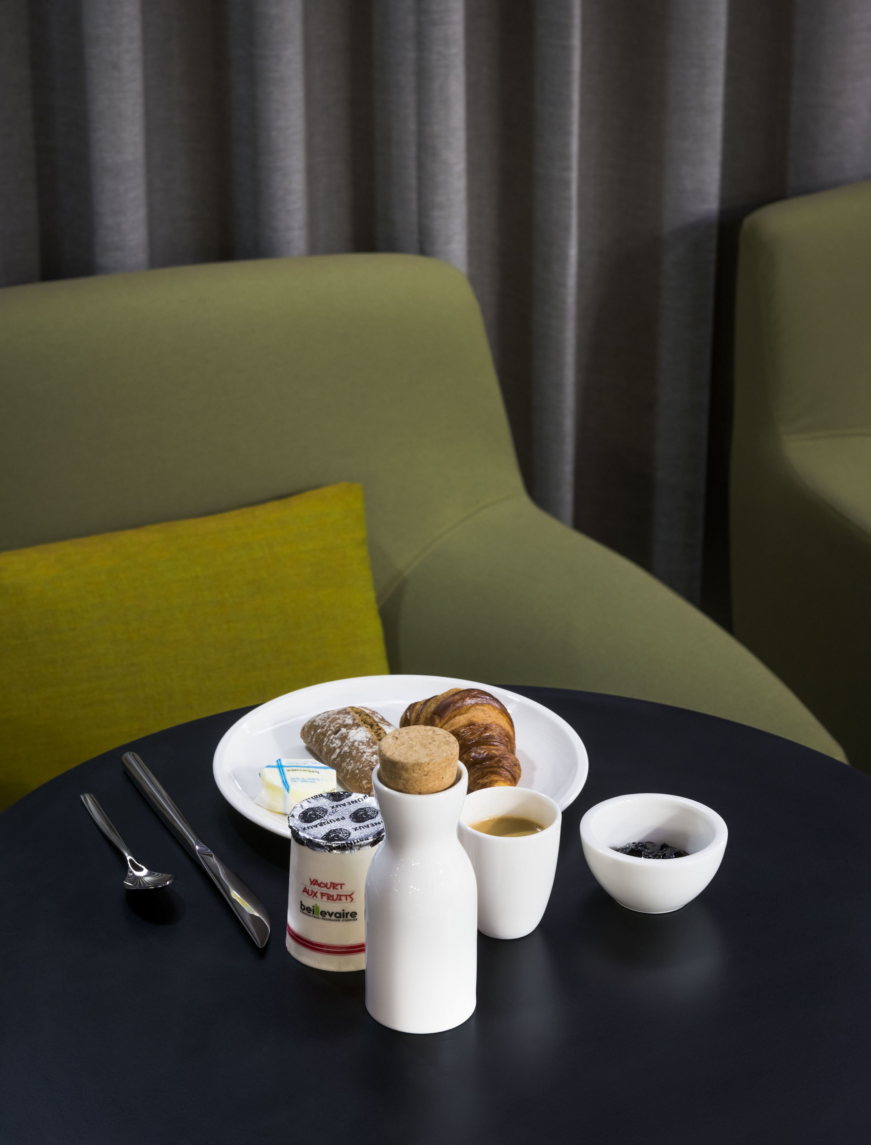 Une table  à manger avec une assiette de pâtisseries, une bouteille de yaourt, une tasse de café et un petit bol de sucre.