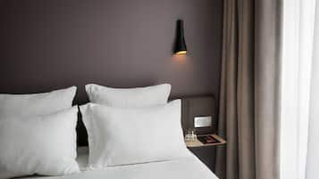 Una cama bien hecha con sábanas blancas, una mesita de noche con un vaso de agua y una lámpara de pared.