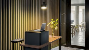 A reception desk with a laptop, a vase with flowers, and a modern interior with vertical wooden panels and recessed lighting. - OKKO Hotels Grenoble Centre (Grenoble)