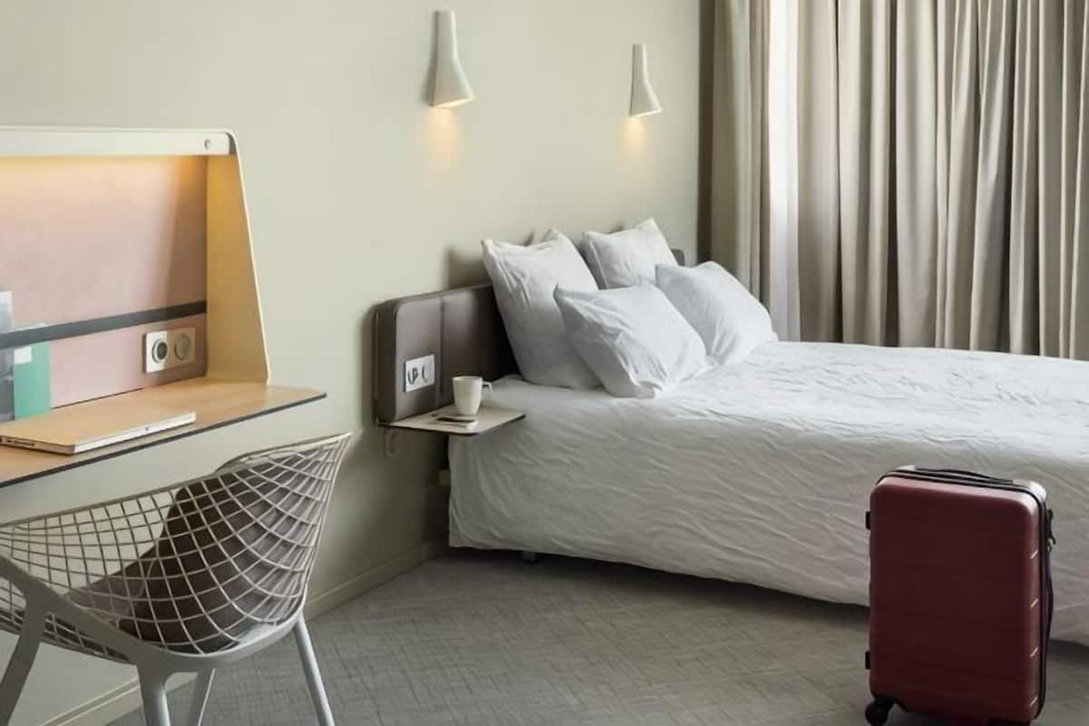 Une chambre dâhĂŽtel avec un lit, un bureau et une chaise, une valise et une lampe.