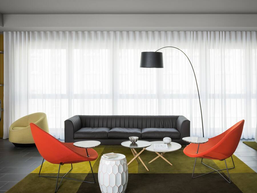 Een moderne woonkamer met een bank, twee rode stoelen, een witte salontafel en een vloerlamp.