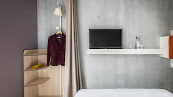 Una habitación de hotel moderna con una cama, un televisor montado en la pared, un armario con estantes y un perchero.