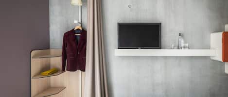 Una habitación de hotel moderna con una cama, un televisor montado en la pared, un armario con estantes y un perchero.