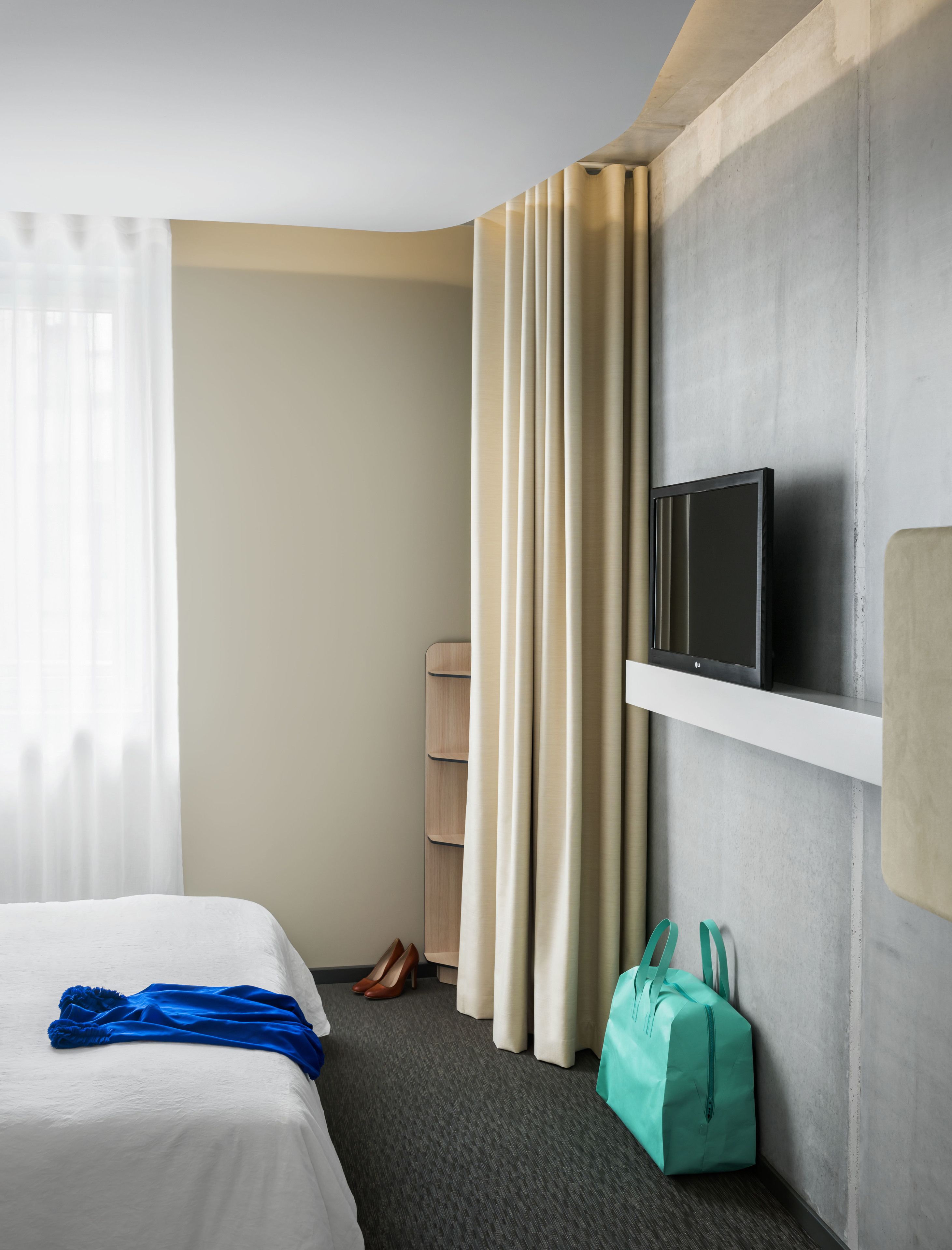 Une chambre d’hôtel avec un lit, un téléviseur fixé au mur, une paire de chaussures et un sac.