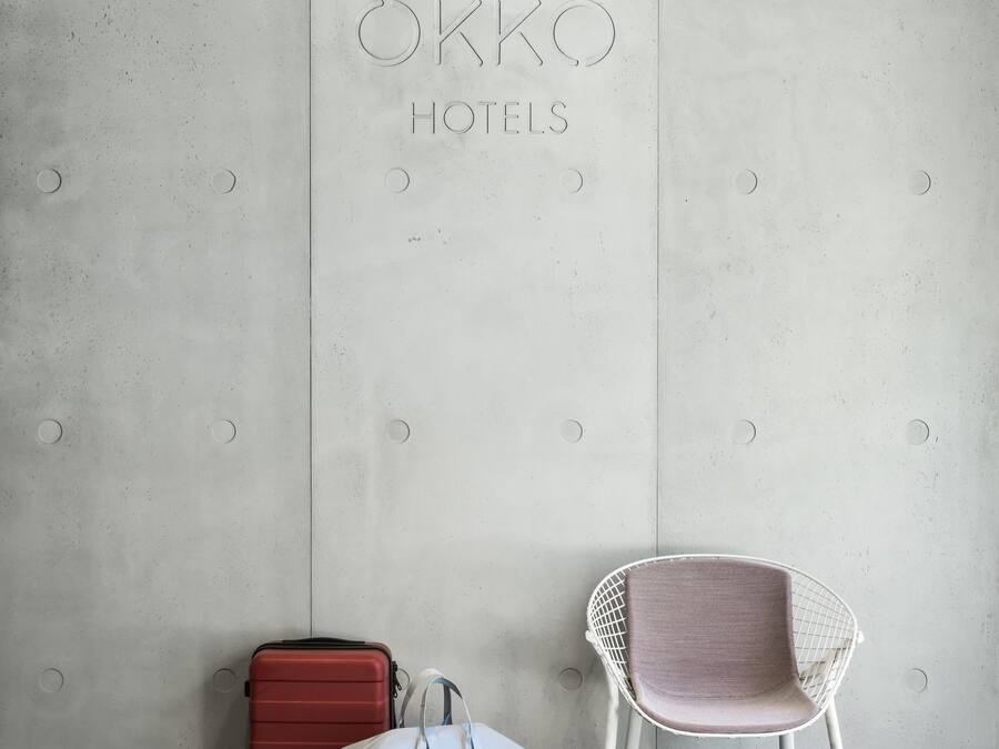 A wall with the inscription "OKKO HOTELS" and a white chair with a pink cushion.