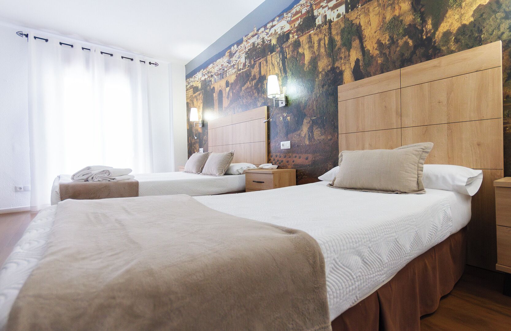 A hotel room with two beds, a wooden headboard, a nightstand, and a wall with a mural.