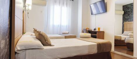 A hotel room with two beds, a flat-screen TV, a mirror, a desk with a chair, and a window with curtains.