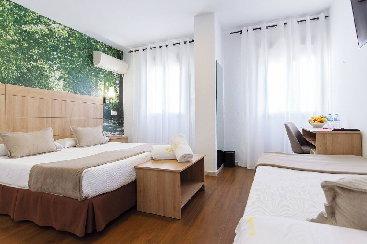Ein Hotelzimmer mit einem Bett, einem Schreibtisch mit Stuhl, einem Spiegel und Blick auf Grünanlagen durch das Fenster.