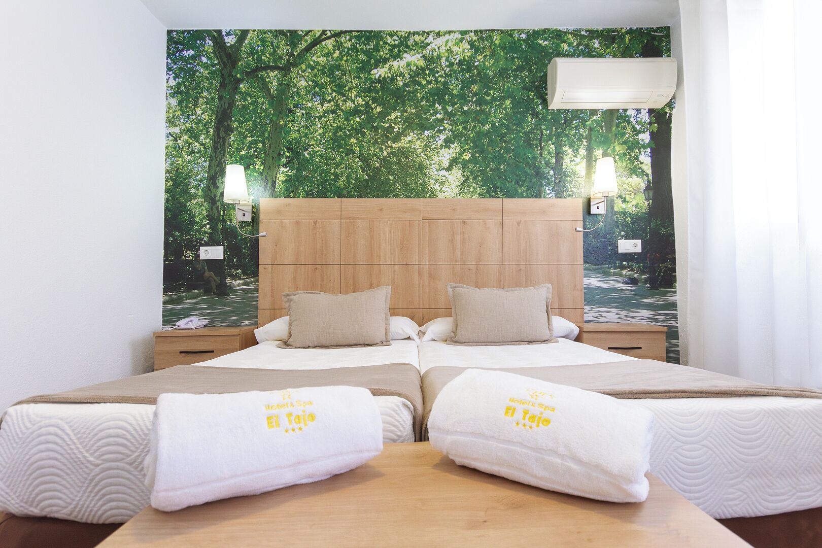Habitación doble con dos camas, cabecera de madera y un mural temático de bosque.