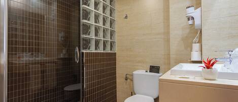 Un baño con cabina de ducha de vidrio, inodoro, lavamanos con espejo y una pequeña planta en maceta.