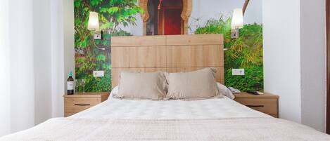 A bedroom with a large bed, wooden headboard, two bedside tables, and a wall mural of greenery and an archway.