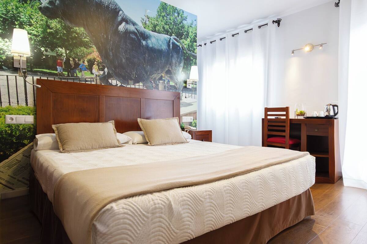 Ein Hotelzimmer mit einem großen Bett, einem Holztisch und einem Wandbild eines Stiers.