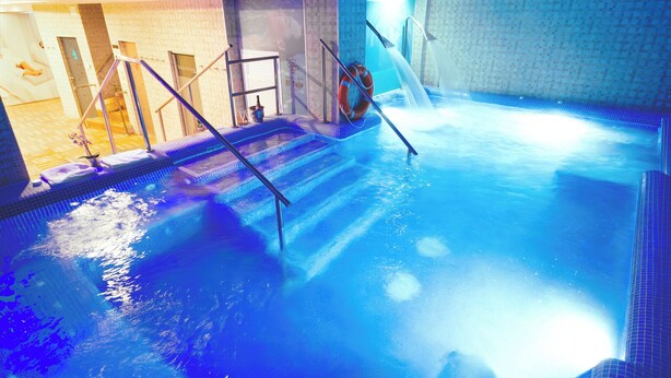 Una piscina interior con superficie de agua cristalina, un trampolín y un muro de azulejos.