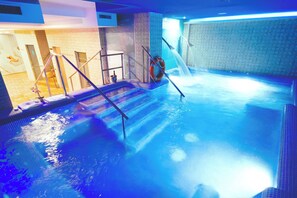 An indoor swimming pool with a clear water surface, a diving board, and a tiled wall. - Hotel El Tajo & SPA (Ronda)
