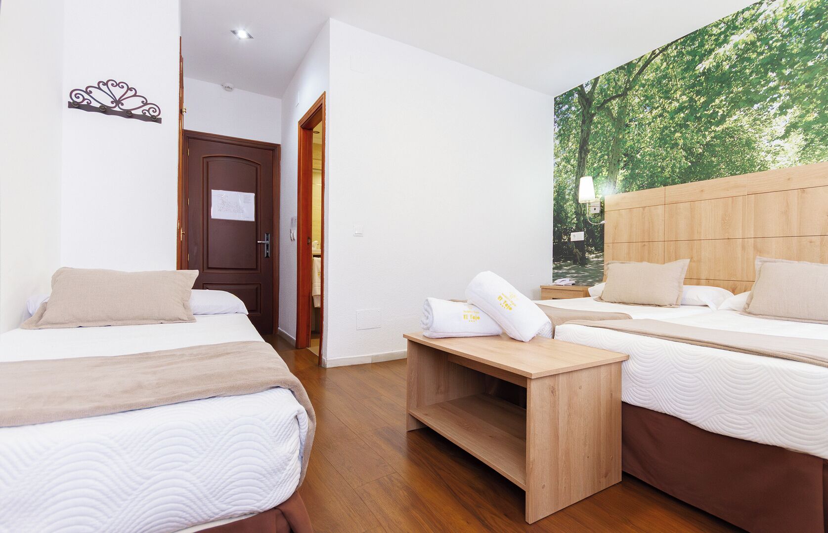 Habitación de hotel con dos camas, una mesita de noche de madera y un gran mural con temática forestal.