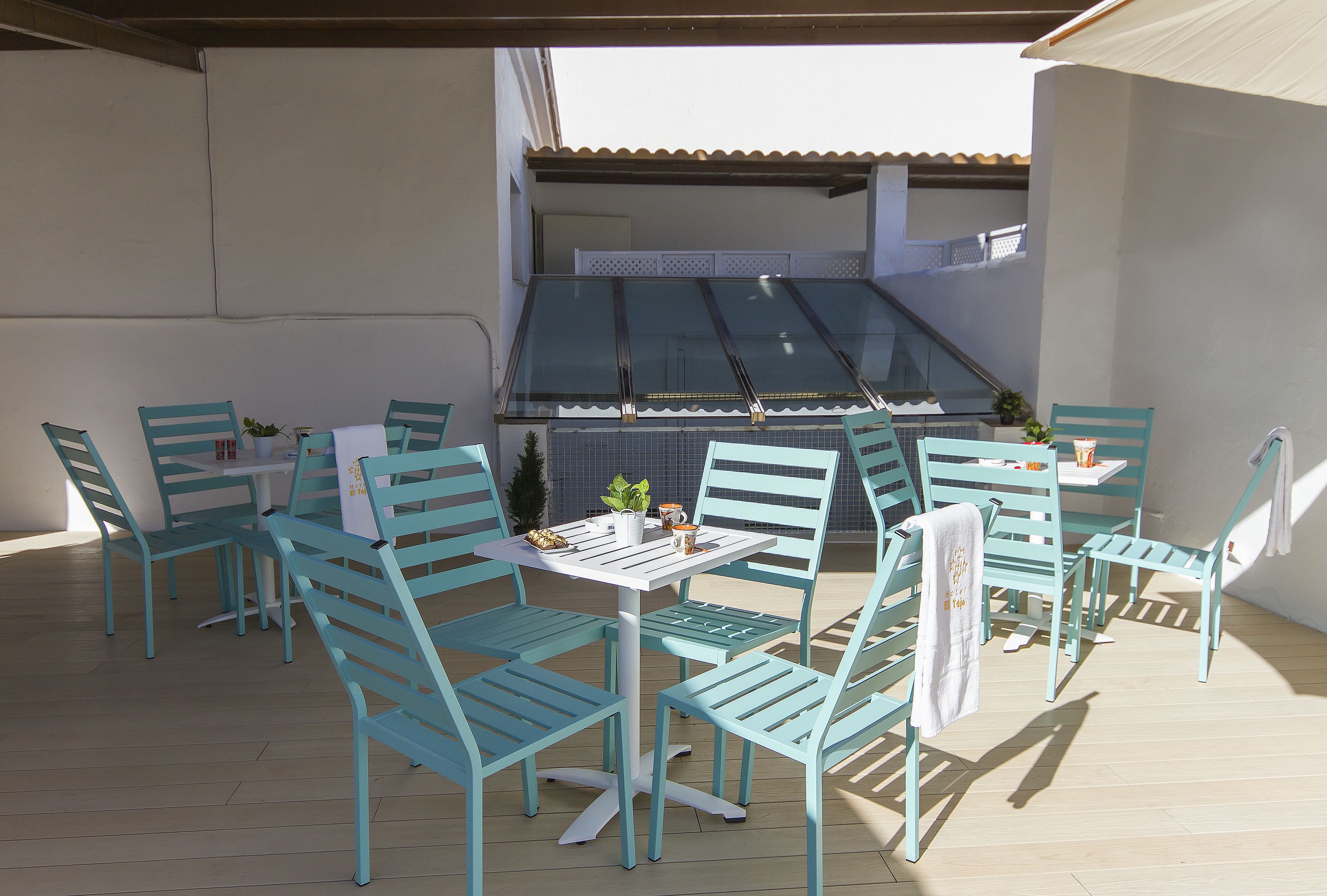 Un patio con sillas turquesa y una mesa blanca, con vistas a un edificio de tejado con azulejos.
