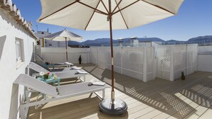 Una terraza en la azotea con sillones de sol, sombrillas y vistas a las montañas.