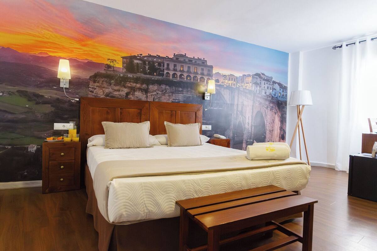 Ein Hotelzimmer mit einem großen Bett, einem hölzernen Kopfteil, Nachttischen, einer Bank, einem Wandbild und einer Stehlampe.