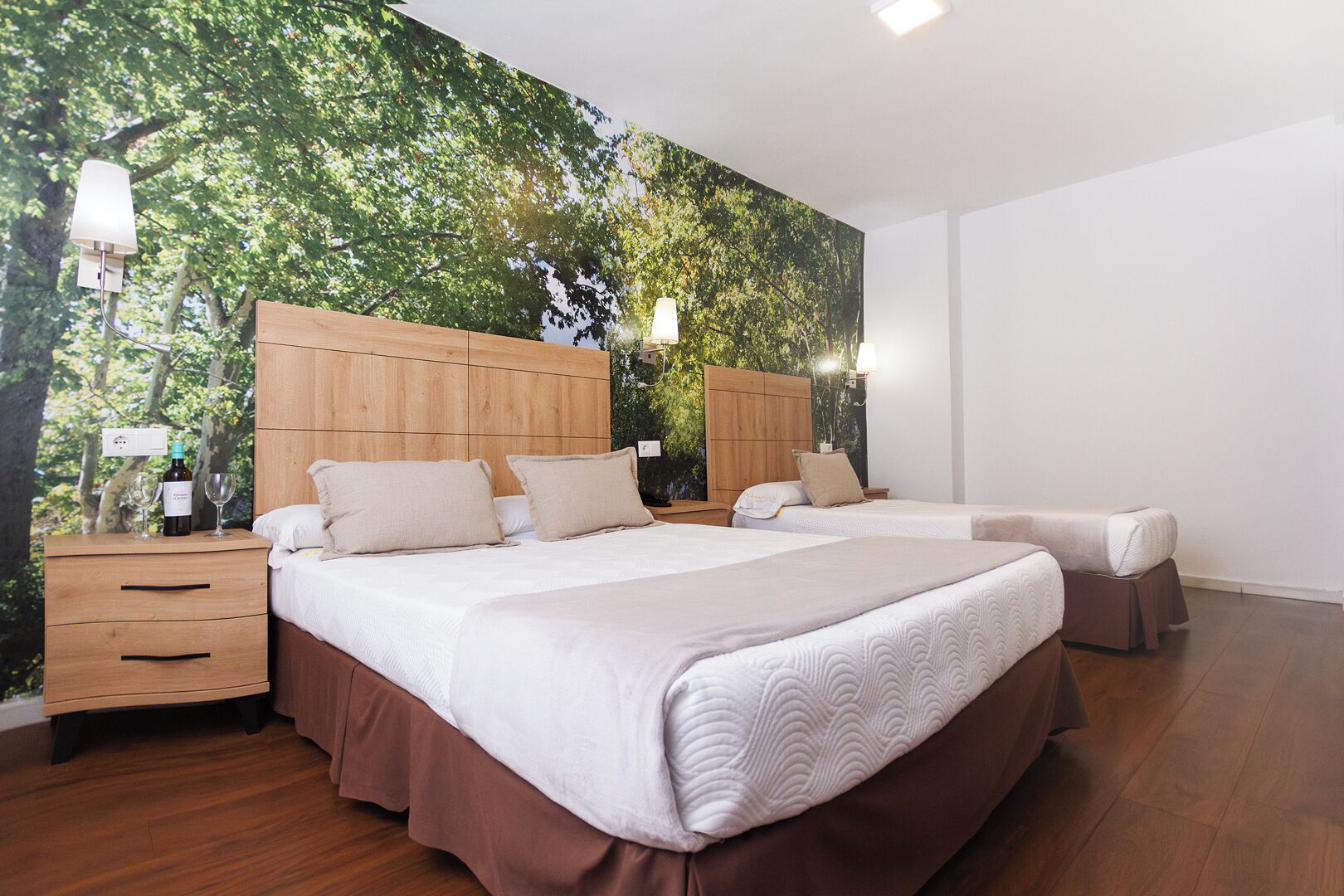 Camera da letto con due letti, testiere in legno, un comodino e un murale raffigurante alberi.