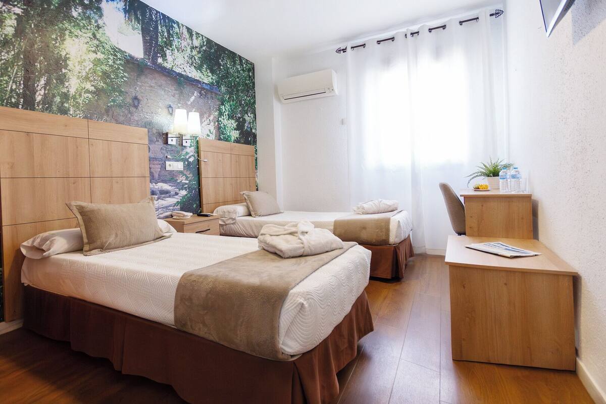 Ein Hotelzimmer mit zwei Betten, einem Schreibtisch, einem Stuhl, einer großen Wandmalerei und einer Klimaanlage.