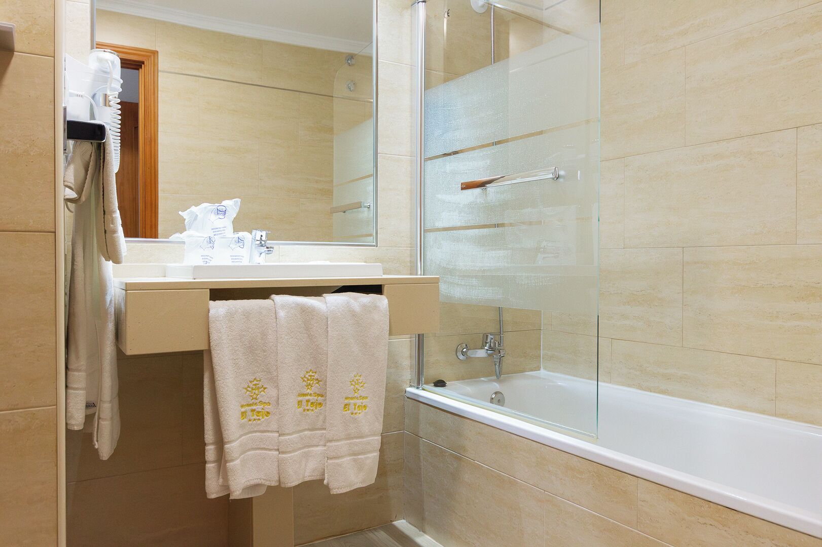 A bathroom with a glass shower enclosure, a white bathtub, and a beige tiled wall.