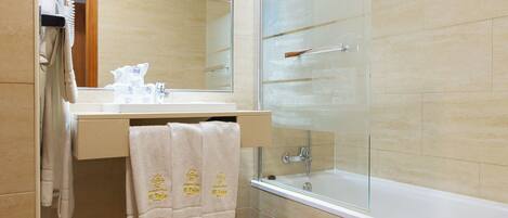 A bathroom with a glass shower enclosure, a white bathtub, and a beige tiled wall.