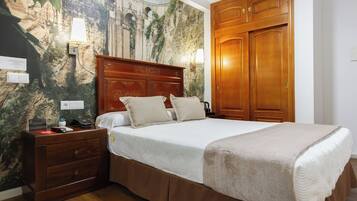 A hotel room with a bed, wooden wardrobe, nightstand, and a wall with a mural.