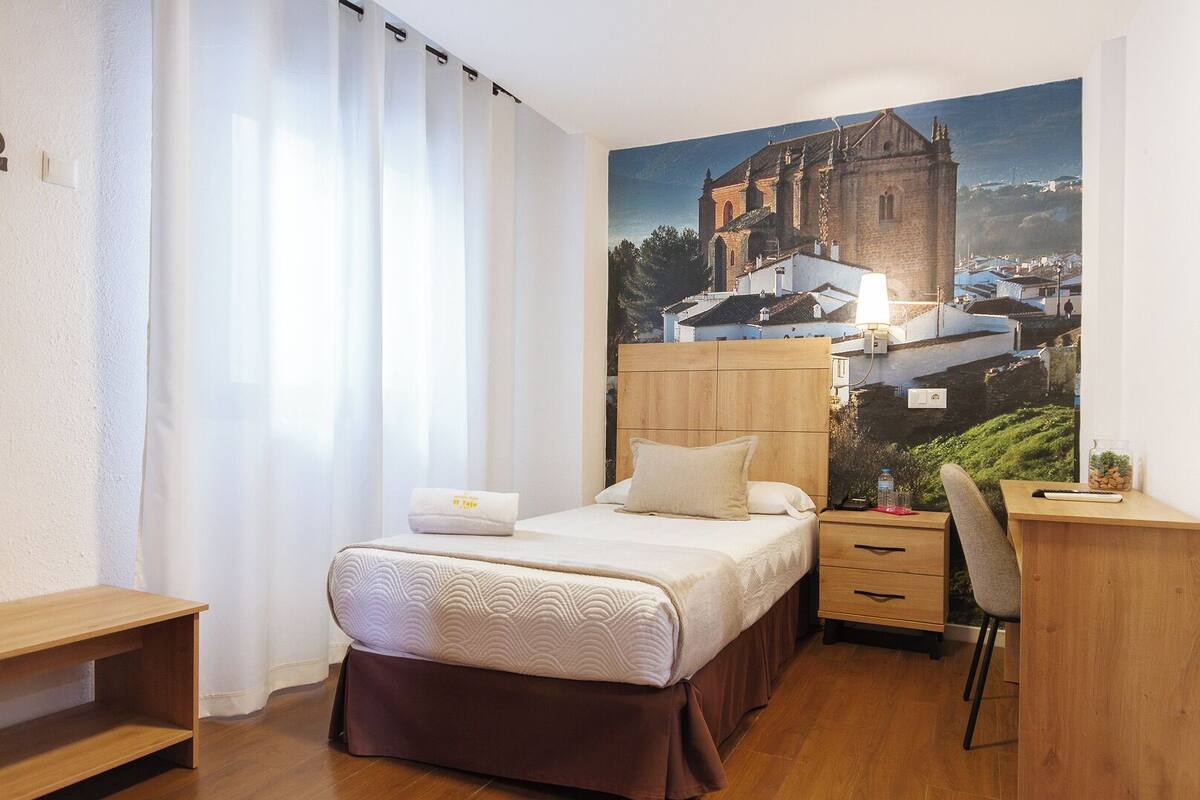 Ein Schlafzimmer mit einem Bett, einem Schreibtisch, einem Stuhl und einem großen Fenster mit Vorhängen.