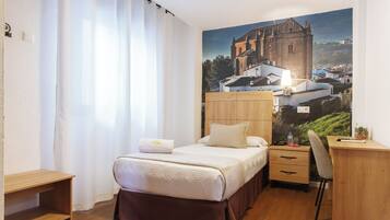 Een slaapkamer met een bed, bureau, stoel en een groot raam met gordijnen.