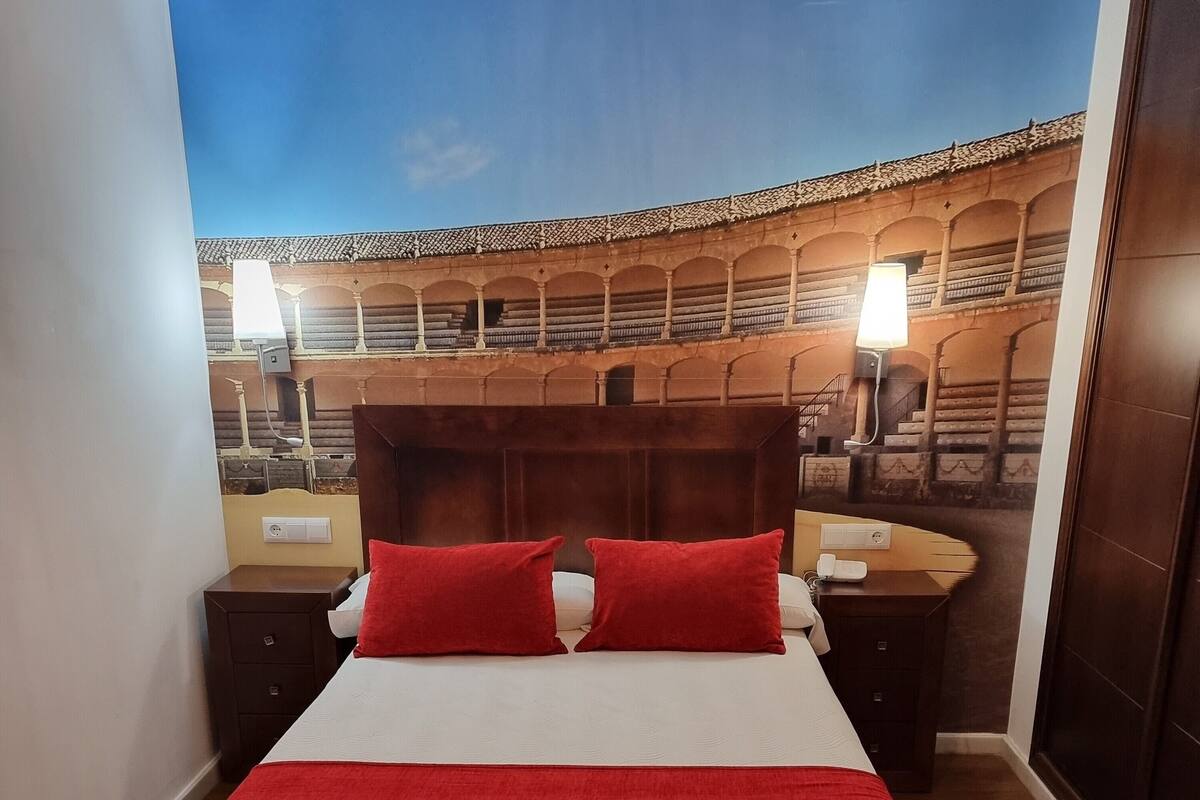 Ein Hotelzimmer mit einem Bett, zwei Nachttischen, einer Bank und einem Wandgemälde.