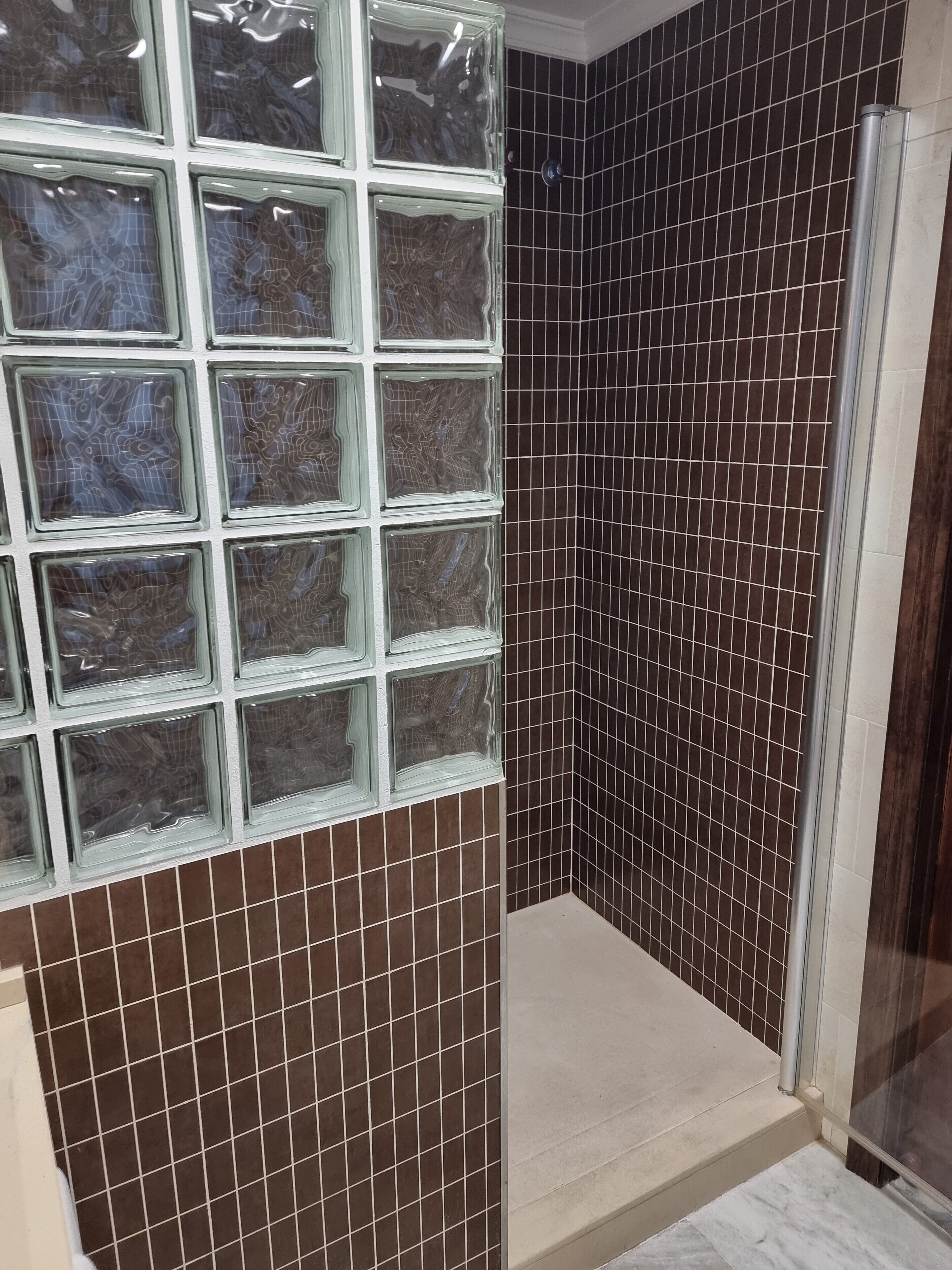A bathroom with a tiled shower area, a glass shower enclosure, and a tiled wall with a geometric pattern.