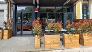 A hotel entrance with a covered entrance, wooden planters with plants, and a sign indicating the hotel name. - Hotel Le Colibri (Aix-les-Bains)