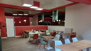 A modern dining area with multiple tables and chairs, a red accent wall, and a large window with a view. - Hotel Le Colibri (Aix-les-Bains)