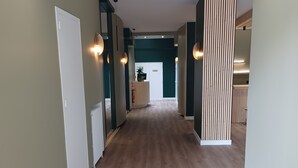 A hallway with wooden flooring, a reception desk, and a door in the distance. - Hotel Le Colibri (Aix-les-Bains)