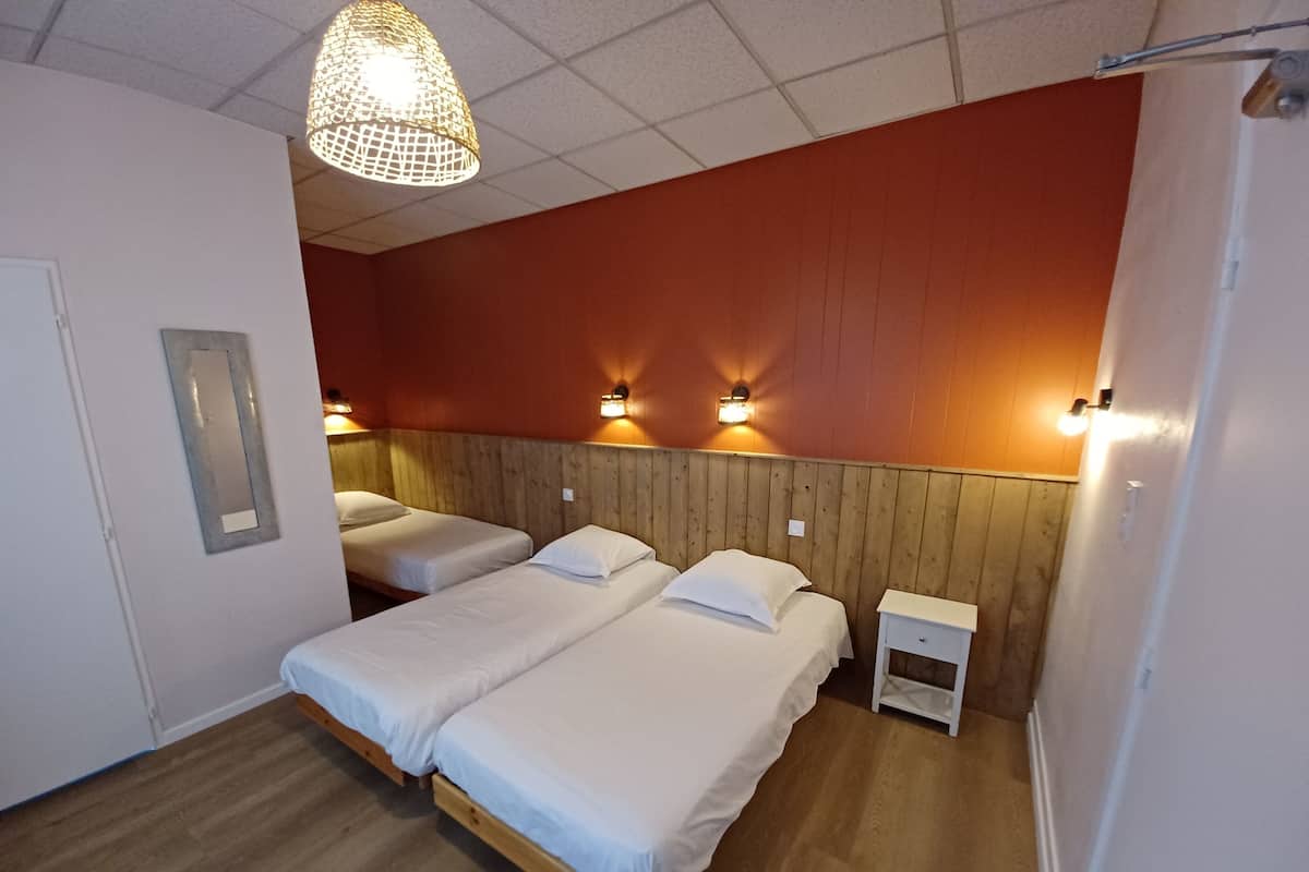 A hotel room with two beds, a wooden headboard, a nightstand, a wall-mounted light fixture, and a hanging light fixture.