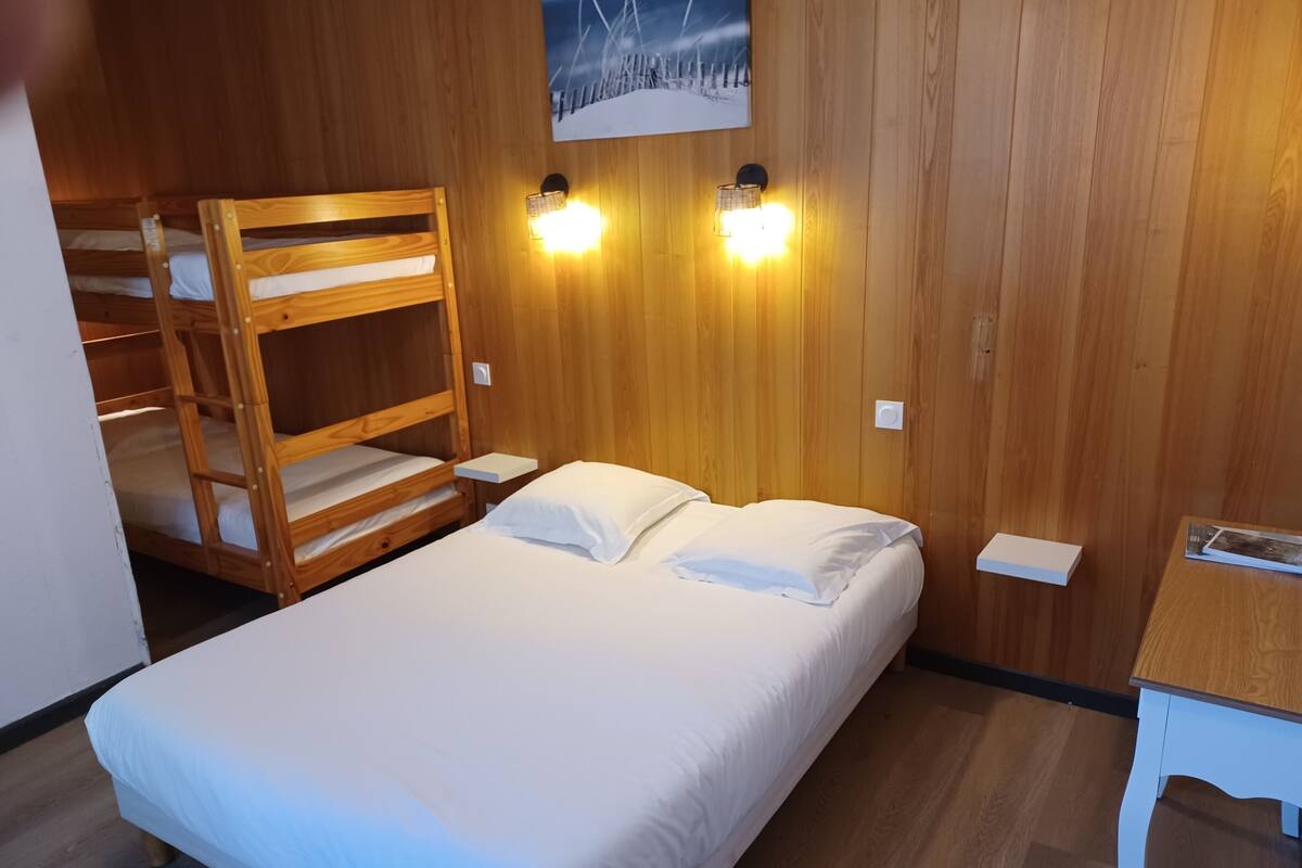 A bunk bed with a white mattress, a single bed with white bedding, wooden walls, two wall-mounted lights, and a framed picture on the wall.