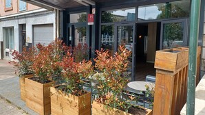 A building entrance with a covered porch, wooden planters with shrubs, and a visible sign with an 'H' symbol. - Hotel Le Colibri (Aix-les-Bains)