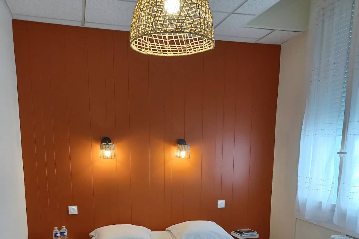 A bedroom with a bed, two wall-mounted lights, a radiator, and a window with curtains.