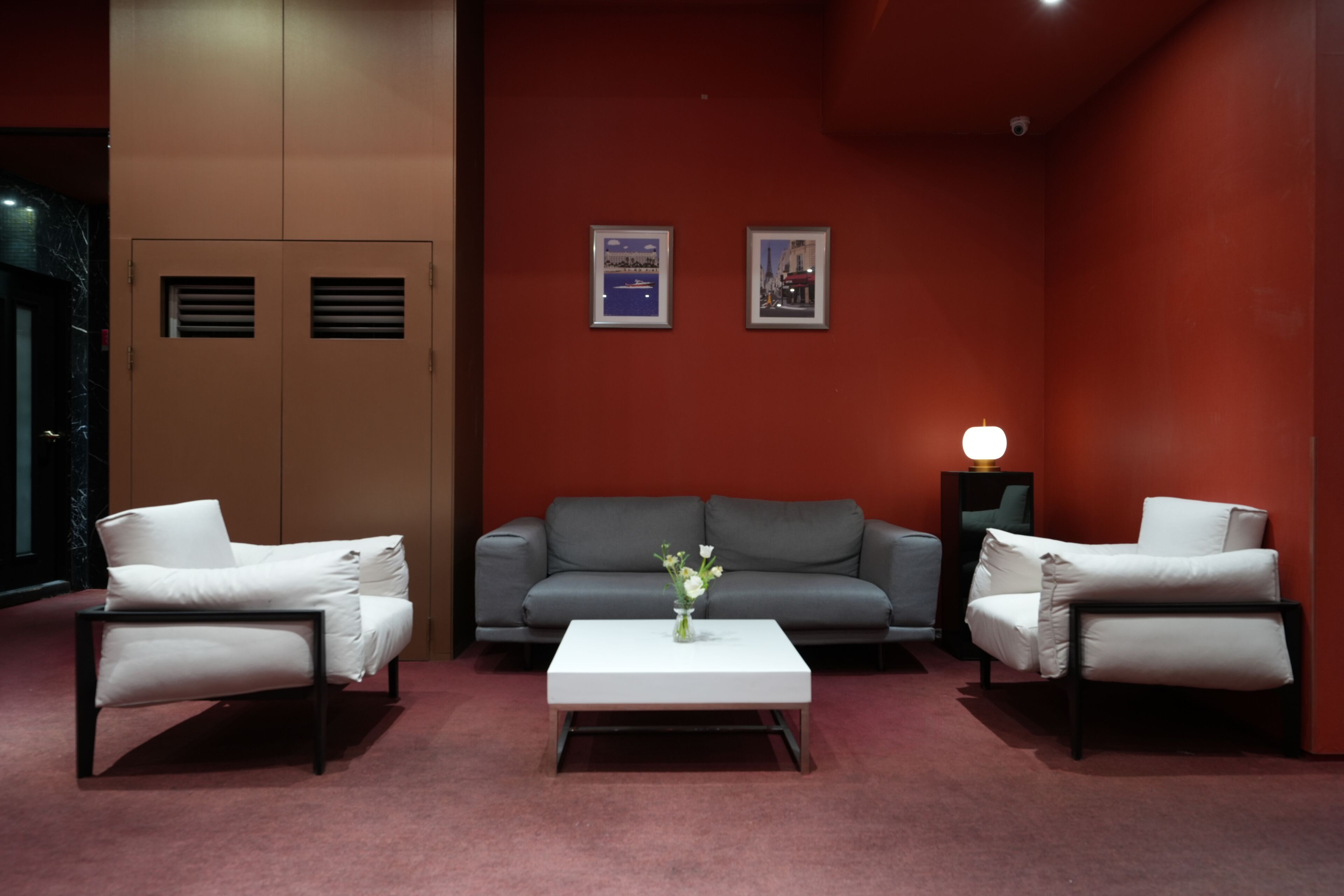 A modern room with a grey sofa, two white armchairs, a white coffee table, and a vase of flowers. There are two framed pictures on the wall and a lamp on a side table.
