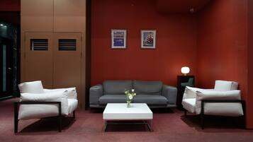 A modern room with a grey sofa, two white armchairs, a white coffee table, and a vase of flowers. There are two framed pictures on the wall and a lamp on a side table.